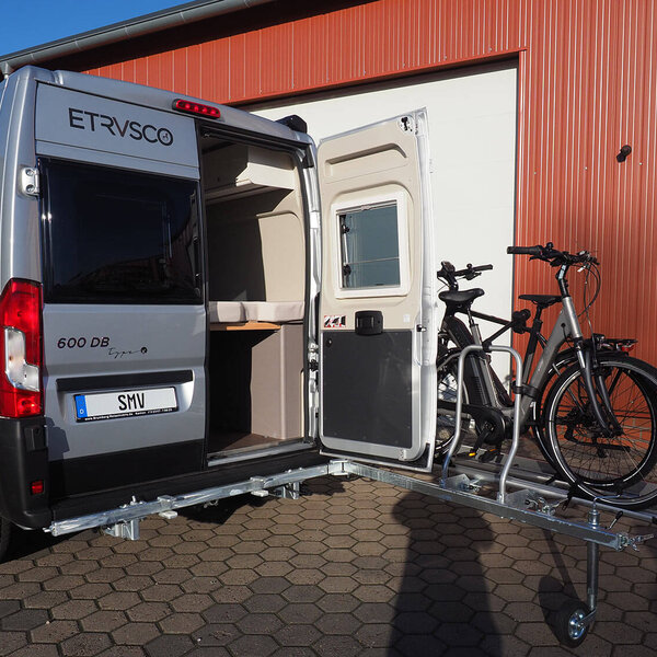 SMV Swing Carry montiert an einem Camper mit frei zugänglicher, geöffneter Hecktür und zwei E-Bikes beladen. 