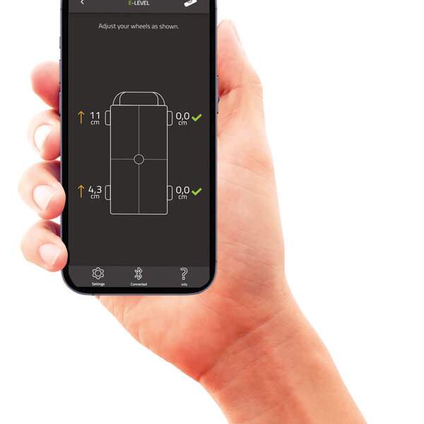 Eine Hand zeigt ein Smartphone mit der E-Trailer App. Darauf das Ausnivellieren eines Campers.