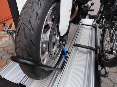 SMV Alu-Star Rolli – Zubehör Fahrradhalterung. Auf der Plattform ist der optionale Rüstsatz für Fahrräder montiert. Darin ist ein Fahrrad befestigt. Daneben auf der Plattform ist das Vorderrad eines Motorrades im Reifenhaltebügel gesichert .